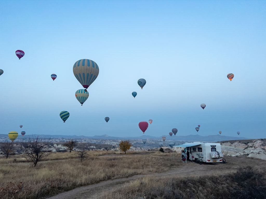 Heißluftballons fliegen über ein geparktes Wohnmobil in der Morgendämmerung